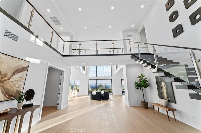 interior space with visible vents, baseboards, wood finished floors, and a towering ceiling