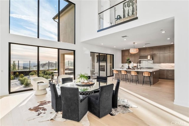 dining space with recessed lighting, light wood-style floors, and a high ceiling