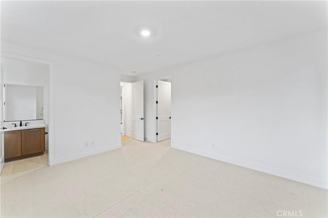 spare room featuring light carpet, baseboards, and a sink