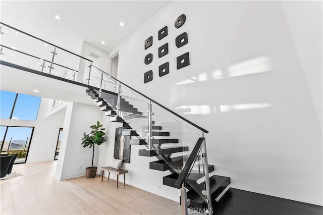 stairs with a high ceiling, wood finished floors, and recessed lighting