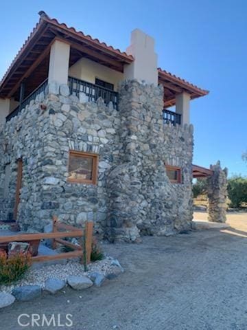 view of side of home featuring a tiled roof, a balcony, stone siding, and a chimney