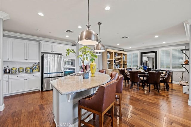 kitchen featuring visible vents, dark wood-style flooring, appliances with stainless steel finishes, a center island with sink, and light stone counters