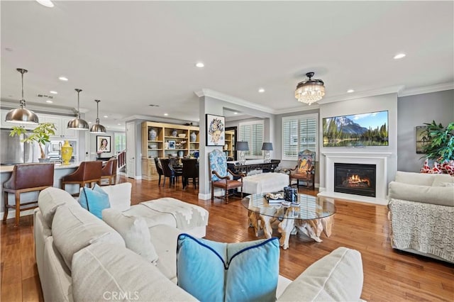 living area with crown molding, recessed lighting, wood finished floors, and a glass covered fireplace