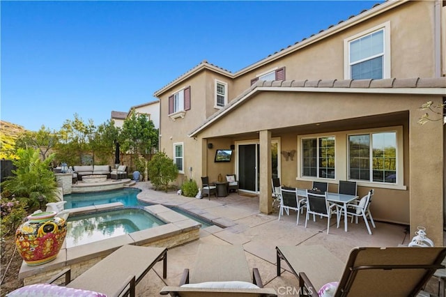 rear view of property with outdoor dining space, a patio, an outdoor hangout area, stucco siding, and an in ground hot tub
