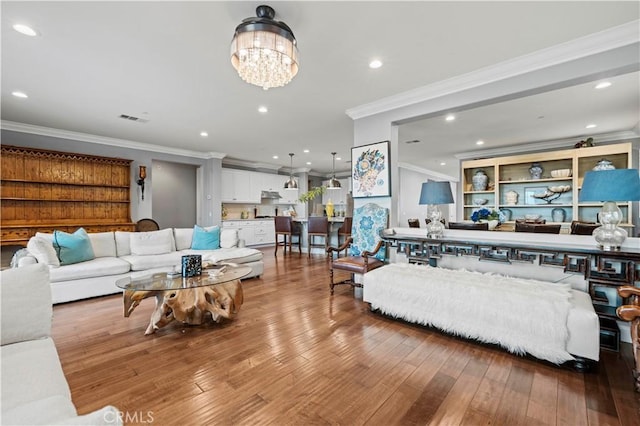 living area with crown molding, hardwood / wood-style floors, a notable chandelier, and recessed lighting