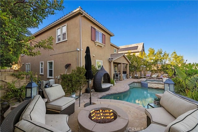 rear view of property with a patio, stucco siding, an outdoor living space with a fire pit, a pool with connected hot tub, and fence