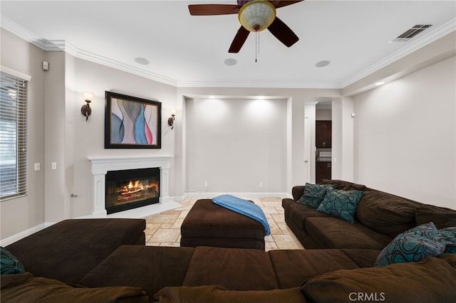 living area with crown molding, stone tile flooring, visible vents, a glass covered fireplace, and a ceiling fan