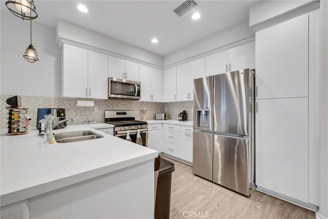 kitchen with appliances with stainless steel finishes, a sink, light countertops, light wood-style flooring, and hanging light fixtures