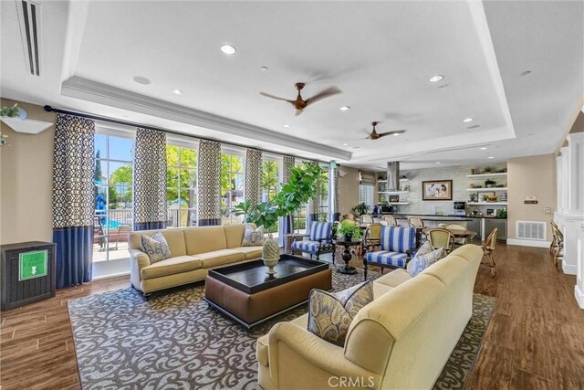 living room with a tray ceiling, a ceiling fan, wood finished floors, recessed lighting, and ornamental molding