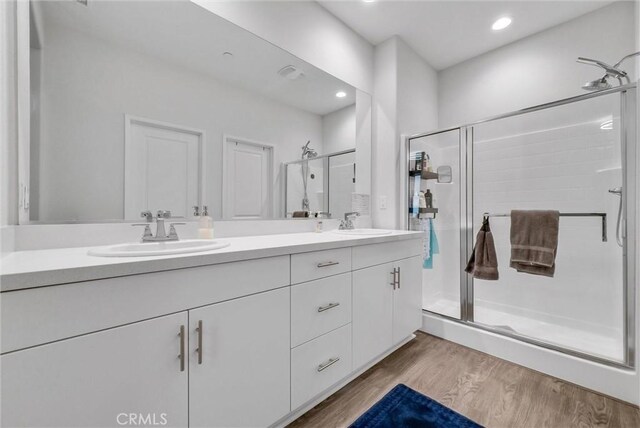 bathroom featuring wood finished floors, a stall shower, double vanity, and recessed lighting