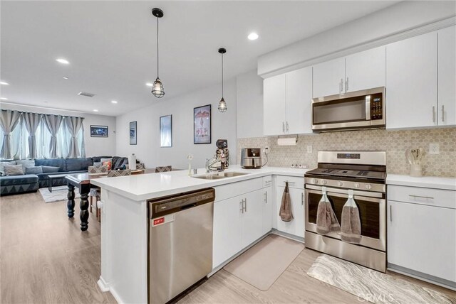 kitchen with appliances with stainless steel finishes, a sink, light wood-style floors, light countertops, and recessed lighting