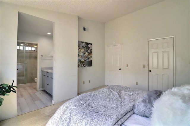 bedroom featuring a textured ceiling, visible vents, light colored carpet, and ensuite bathroom