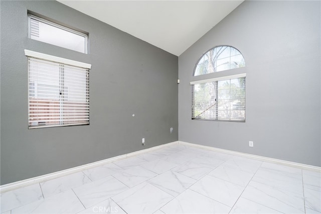 empty room featuring high vaulted ceiling, marble finish floor, and baseboards