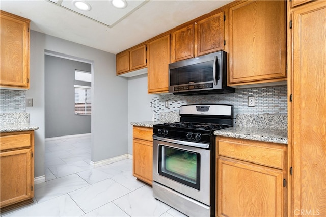 kitchen with light stone countertops, tasteful backsplash, appliances with stainless steel finishes, marble finish floor, and baseboards