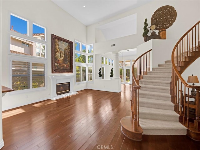 125 Heath Meadow Pl, Simi Valley, CA 93065 - unfurnished living room with stairs, wood-type flooring, a glass covered fireplace, ornate columns, and a high ceiling