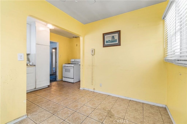 kitchen with white cabinets, white gas range oven, baseboards, and light tile patterned flooring