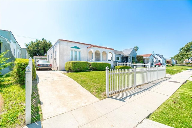 mediterranean / spanish-style home with concrete driveway, a residential view, stucco siding, a fenced front yard, and a front yard