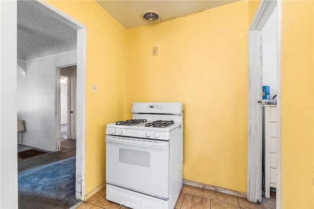 kitchen with white gas stove, a textured ceiling, visible vents, light tile patterned flooring, and baseboards