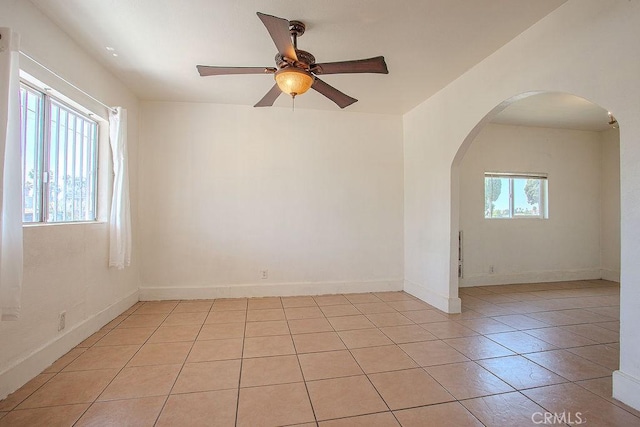 unfurnished room with baseboards, arched walkways, a ceiling fan, and light tile patterned floors