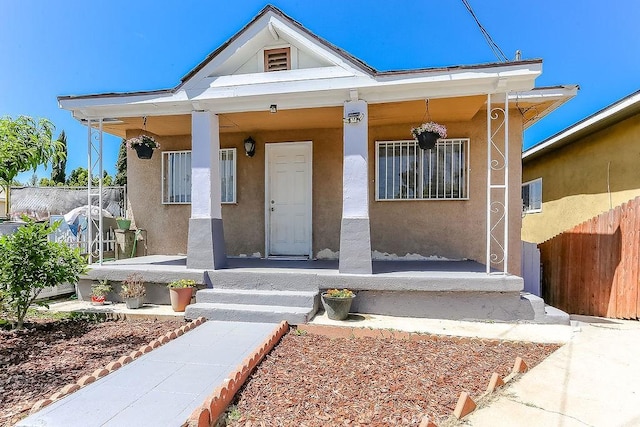bungalow-style house with fence, covered porch, and stucco siding