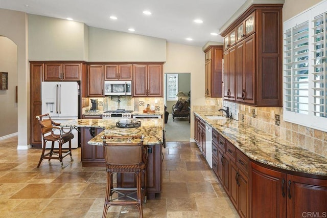 1034 Via Reata, Vista, CA 92081 - kitchen featuring a center island, a sink, white appliances, arched walkways, and light stone countertops