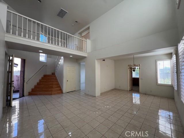 unfurnished living room with a towering ceiling, visible vents, light tile patterned flooring, stairs, and a notable chandelier