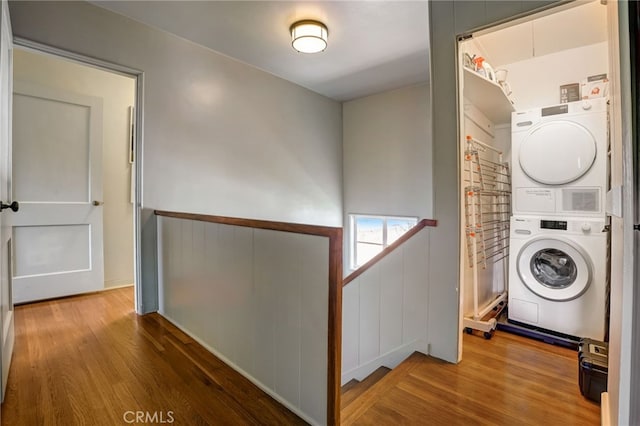 laundry area with stacked washer / dryer, laundry area, a wainscoted wall, and wood finished floors