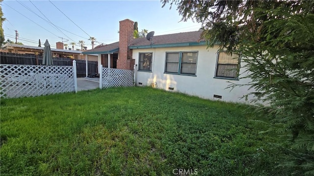 rear view of house with a chimney, fence, a yard, stucco siding, and crawl space