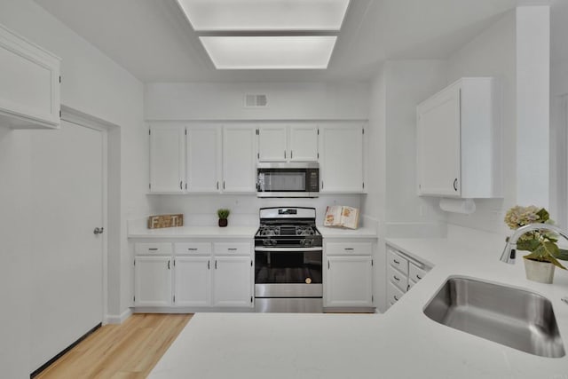 kitchen with light wood-style flooring, light countertops, white cabinets, stainless steel appliances, and a sink