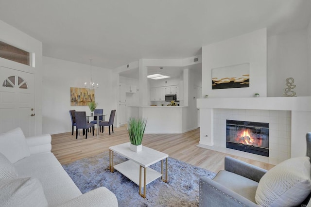 living room featuring a chandelier, a tile fireplace, light wood-style floors, and visible vents