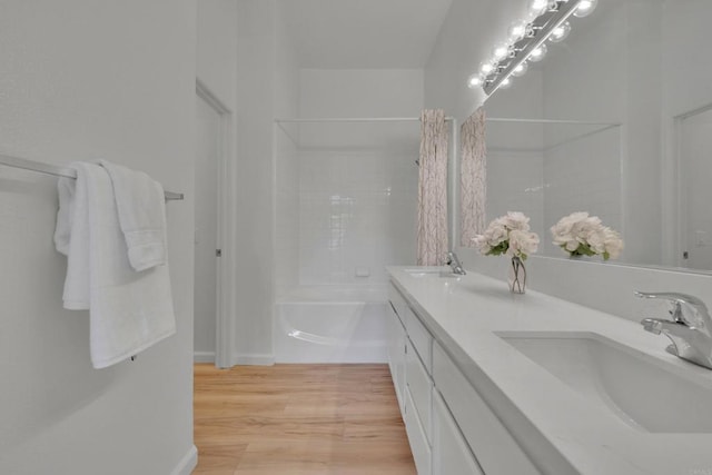 bathroom with a sink, a bath, double vanity, and wood finished floors