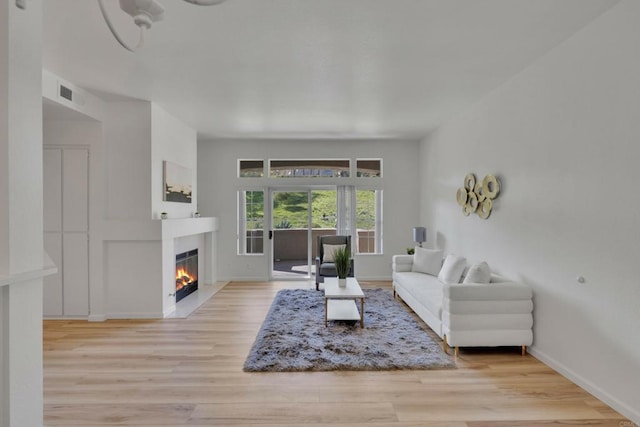living area with wood finished floors, visible vents, baseboards, and a warm lit fireplace