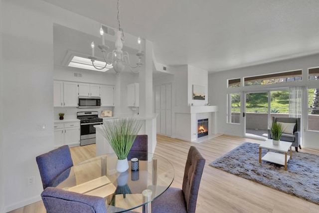 dining space featuring visible vents, a glass covered fireplace, a chandelier, and light wood-style floors