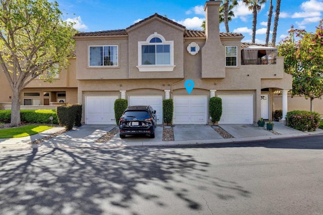 townhome / multi-family property with a chimney, an attached garage, driveway, and stucco siding
