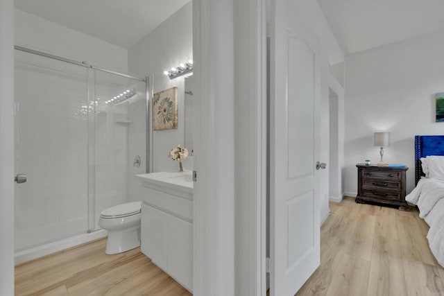 ensuite bathroom with toilet, vanity, a stall shower, and wood finished floors