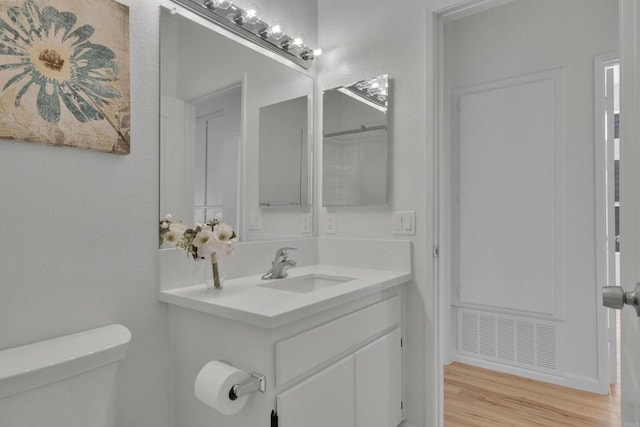 bathroom with vanity, visible vents, toilet, wood finished floors, and a textured wall