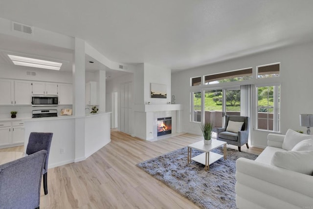 living area featuring visible vents, light wood finished floors, and a fireplace