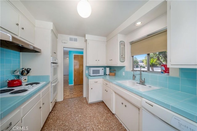 kitchen featuring white appliances, white cabinets, visible vents, a sink, and backsplash