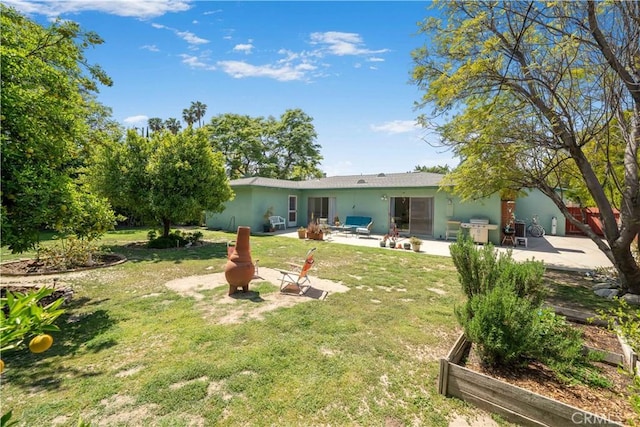 rear view of property featuring a patio area, a garden, stucco siding, and a yard