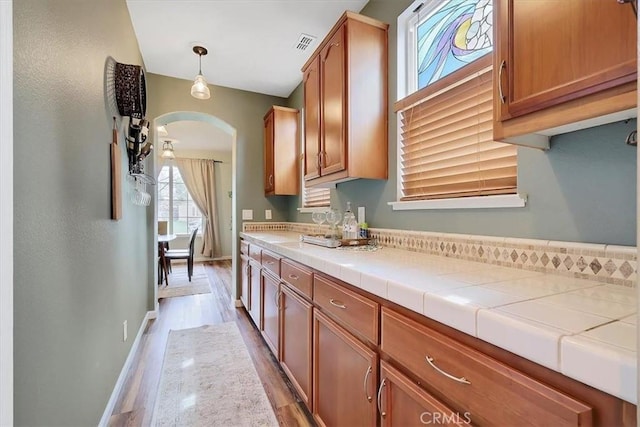 kitchen featuring baseboards, light wood-style flooring, visible vents, brown cabinets, and arched walkways