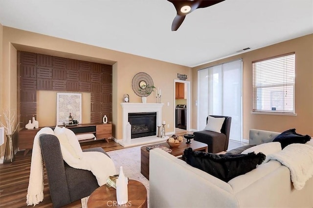 living room with a ceiling fan, a glass covered fireplace, visible vents, wood finished floors, and baseboards