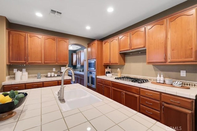 kitchen with visible vents, arched walkways, a sink, stainless steel appliances, and tile countertops