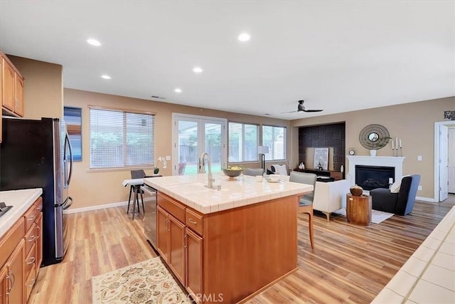 kitchen featuring appliances with stainless steel finishes, tile counters, ceiling fan, light wood finished floors, and a sink