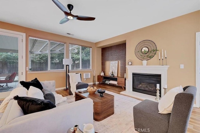 living room featuring visible vents, ceiling fan, a glass covered fireplace, and wood finished floors