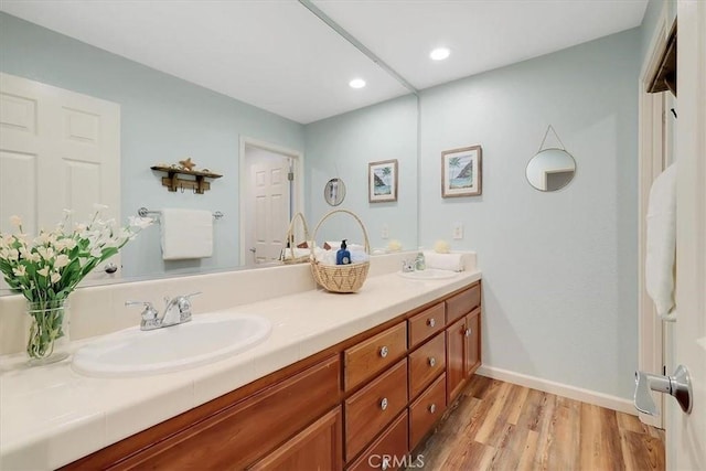 bathroom with wood finished floors, double vanity, a sink, and baseboards