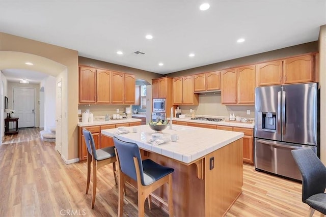 kitchen with light wood-type flooring, a center island, visible vents, appliances with stainless steel finishes, and arched walkways