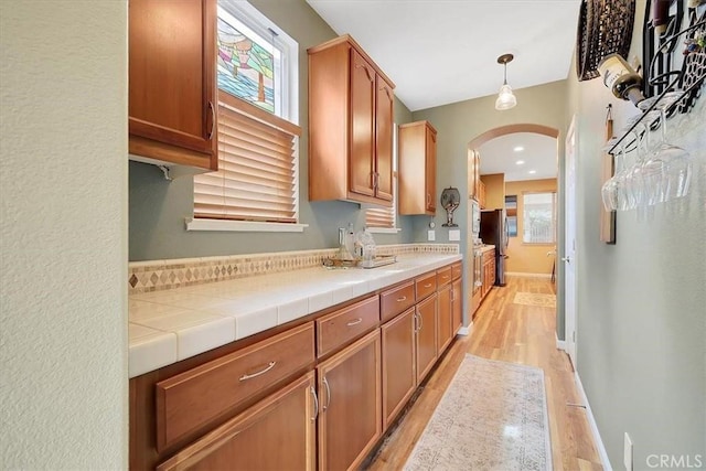 kitchen with baseboards, arched walkways, decorative light fixtures, brown cabinets, and light wood finished floors