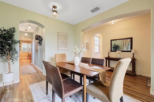 dining area featuring light wood-style floors, arched walkways, visible vents, and baseboards