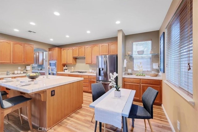 kitchen with arched walkways, appliances with stainless steel finishes, light wood finished floors, and light brown cabinets
