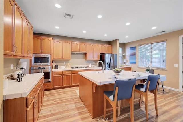 kitchen featuring a kitchen breakfast bar, light wood-style flooring, visible vents, stainless steel appliances, and tile countertops